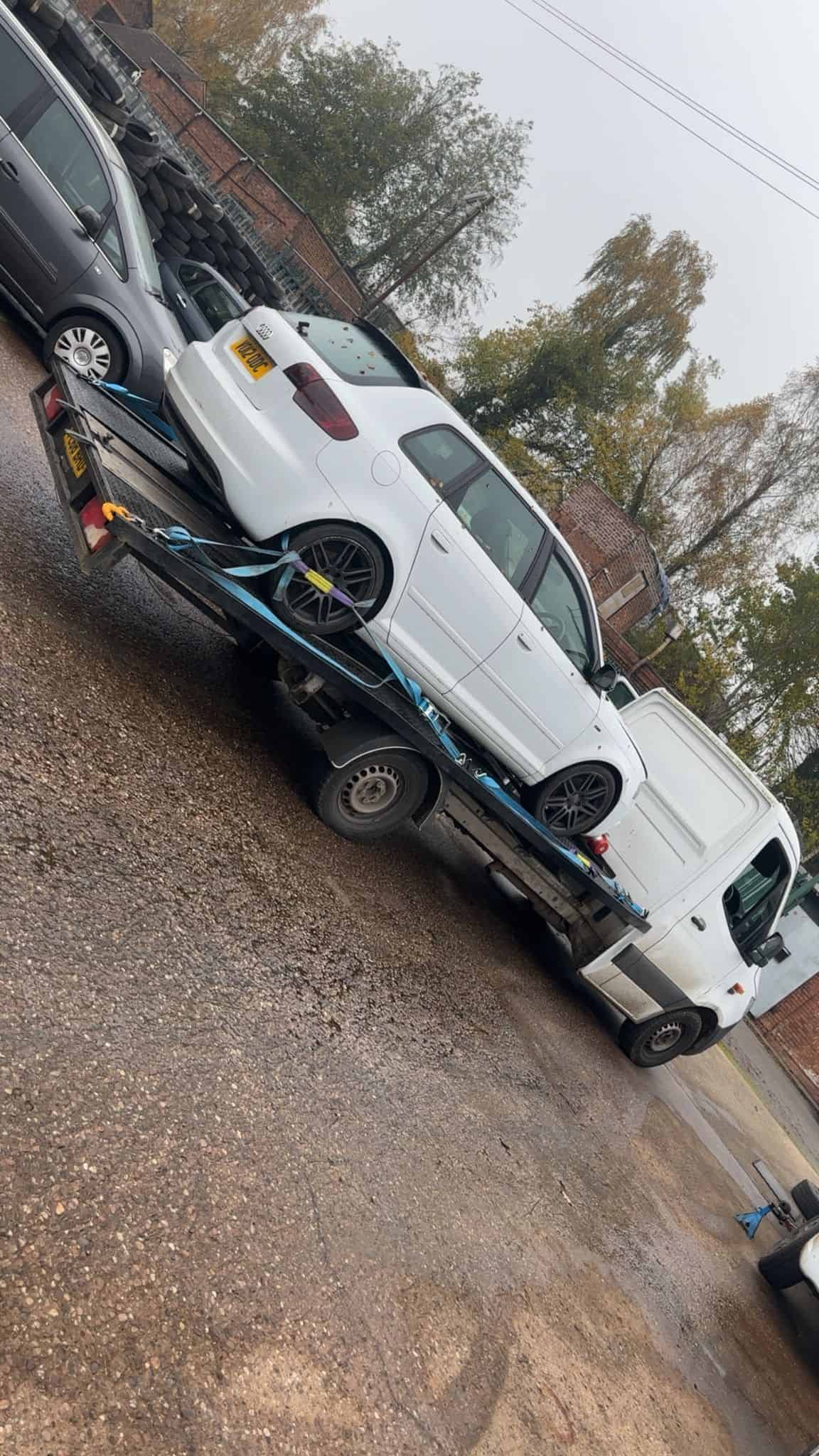 Car recovery truck transporting a white sports car on a flatbed.